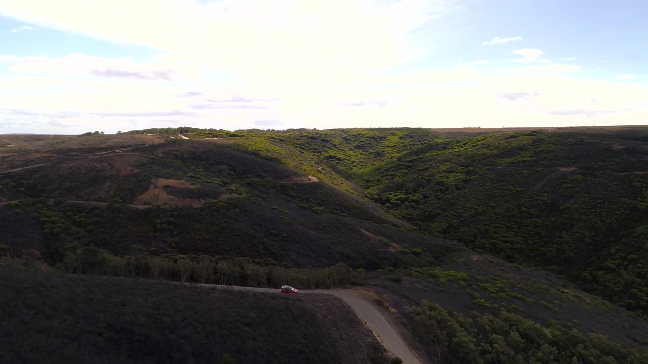 coche rojo conduciendo una sola carretera gente saludando fuera de ella tabla de surf en el techo superior volando antena delante de