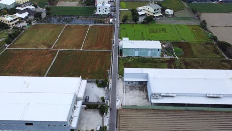 expansive agricultural fields next to industrial warehouses under cloudy skies, daytime, aerial view