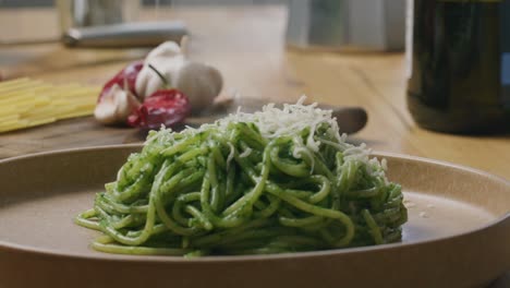 grating cheese over hot pasta with spinach sauce on plate