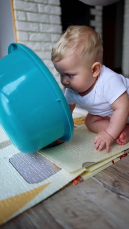 curious little baby crawls by the floor at home. parent puts a washbowl on kid's head and child smiles. vertical video.
