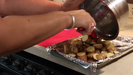 Primer-Plano-De-Una-Mujer-Poniendo-Papas-Baby-En-Rodajas,-Aceitadas-Y-Sazonadas-En-Una-Sartén-Para-Asar-En-Una-Cocina-De-Rv