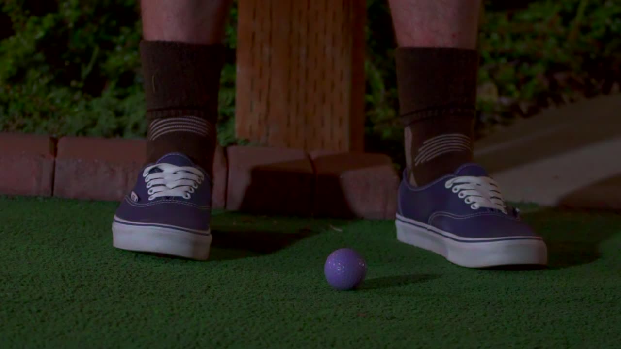 A slow motion close up of a purple mini golf ball getting hit with a club