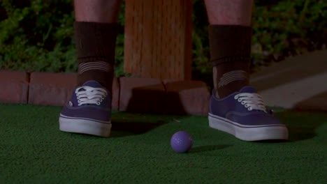 a slow motion close up of a purple mini golf ball getting hit with a club