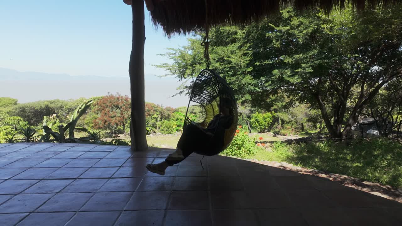A Woman Is Relaxing On A Hanging Egg Chair Outdoor. Static Shot