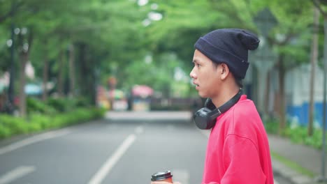 happy young asian freelancer wear beanie hat and headphones on neck, walking on pedestrian crossing in city