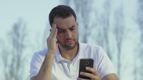 un joven barbudo cansado mirando su teléfono inteligente.