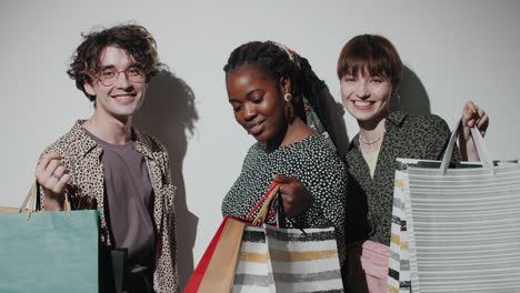 amigos positivos diversos posando con bolsas de compras en el estudio