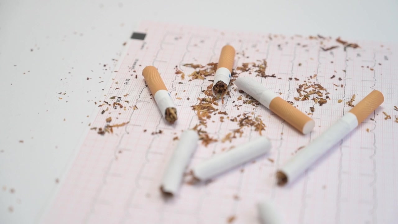 Cigarros quebrados e tabaco caindo sobre um papel de ECG, representando os perigos do tabagismo.