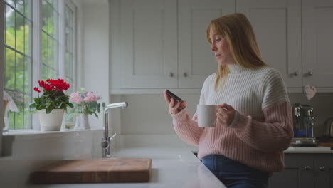 worried woman looking at smart meter in kitchen at home during cost of living energy crisis