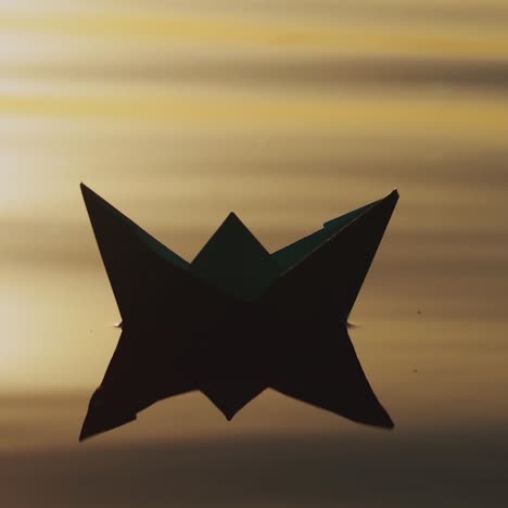 paper boat by handmade is floating on the waves of the river at sunset. the image of a paper ship is reflecting in the water in the evening