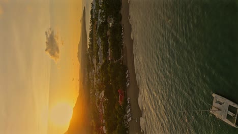 Toma-Aérea-De-Acercamiento-De-Un-Catamarán-Anclado-En-La-Bahía-De-La-Ciudad-De-Playa-Dorada-Durante-La-Puesta-De-Sol-Dorada---Toma-Vertical