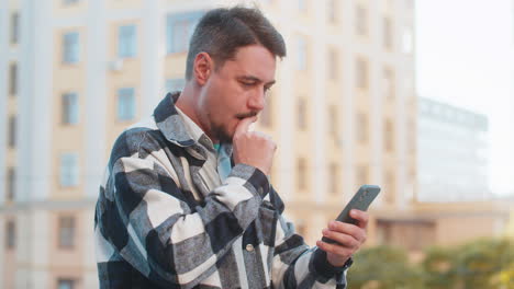 happy young man using smartphone celebrating victory win good message news on downtown city street