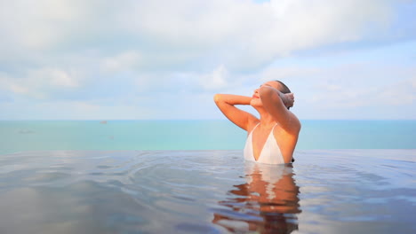 Young-woman-emerging-from-infinity-pool-and-strokes-her-wet-hair