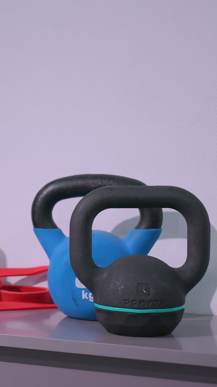 Kettlebell, tali resistensi, cakram keseimbangan, dan peralatan gym lainnya tertata rapi di rak di studio kebugaran, menciptakan ruang yang terorganisir untuk latihan kekuatan dan latihan inti