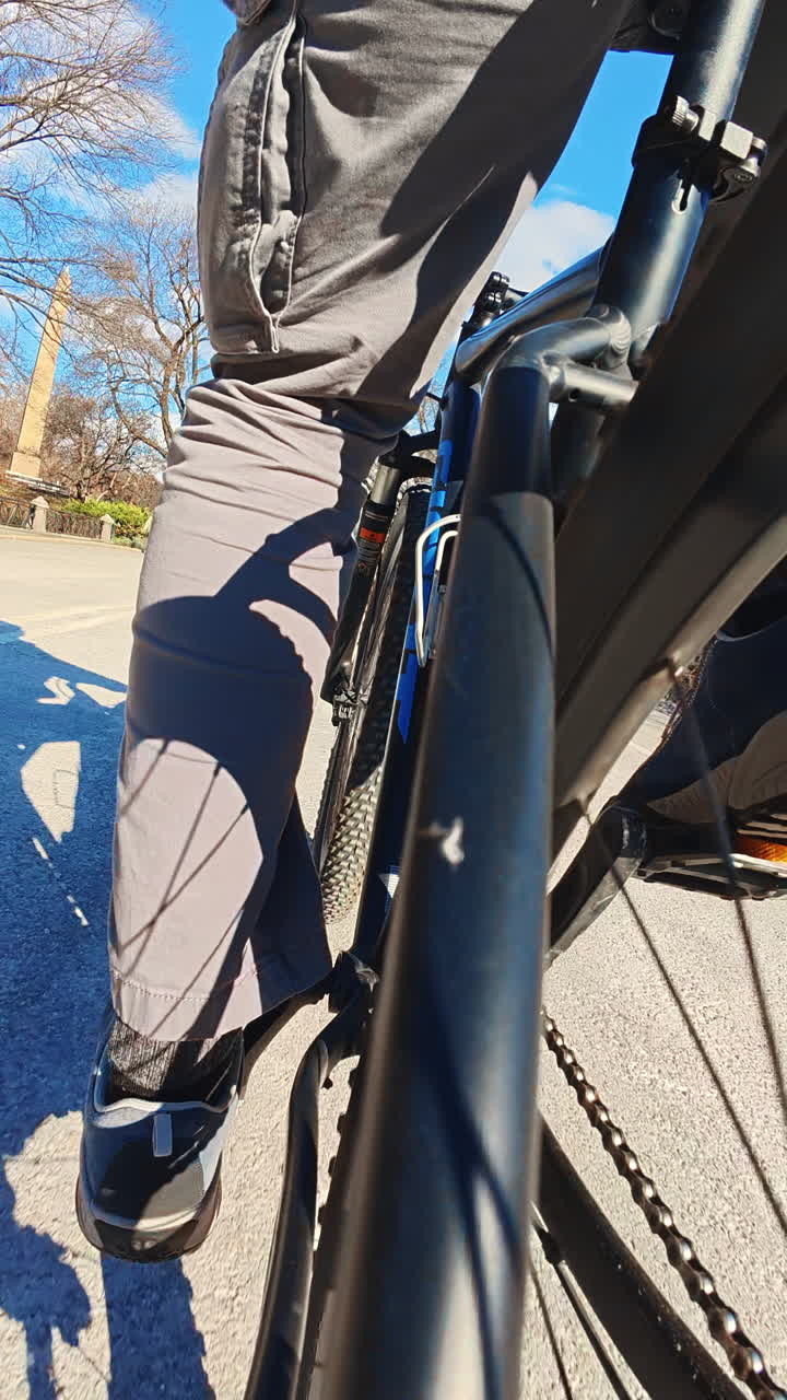 New York, USA, 25 December 2025: Low angle perspective of a cyclist riding a bicycle. Close-up low angle view of a person's leg and the frame of a bicycle while riding on a paved road