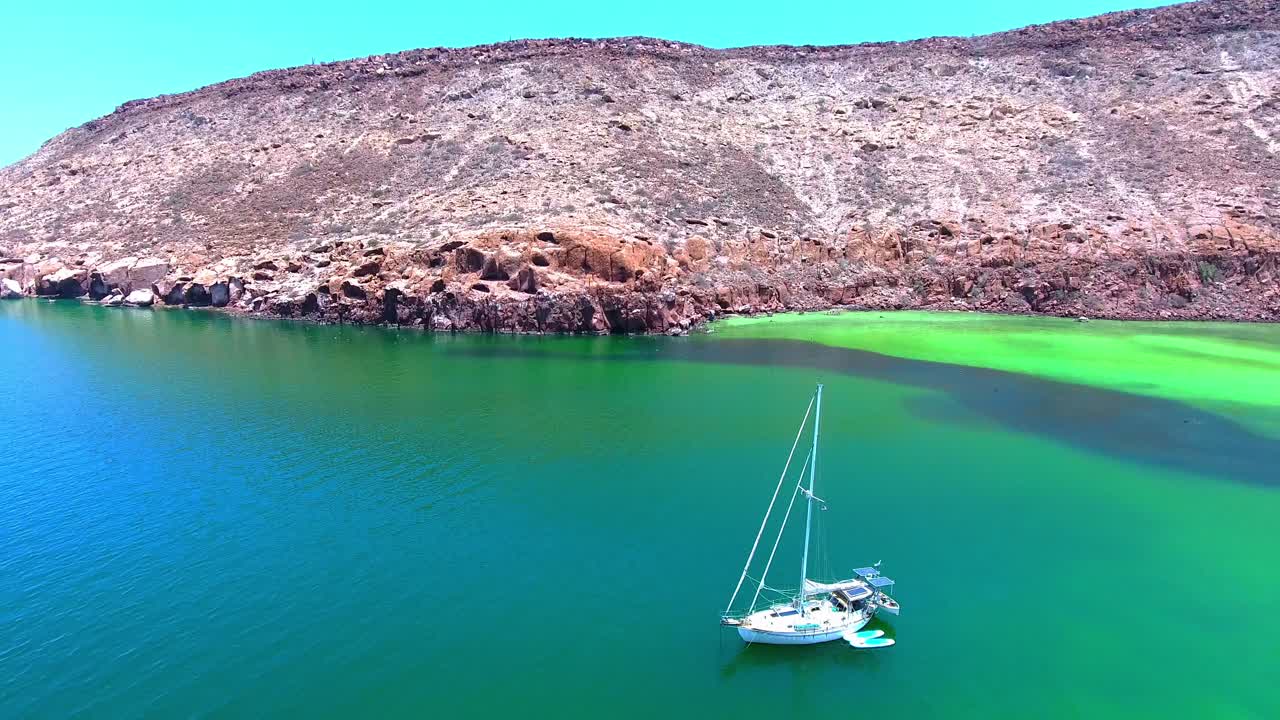 무인도 해안 근처의 에메랄드 만에 정박된 범선의 드론 전망