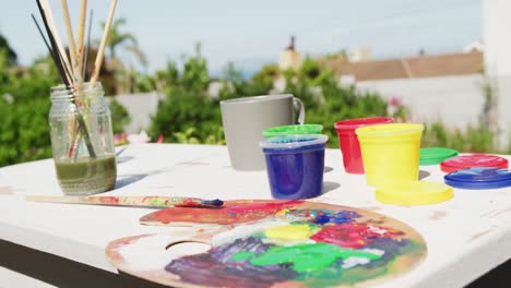 Close-up-of-colourful-paints-and-painting-equipment-lying-on-table-in-garden