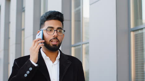 Indian-businessman-having-remote-conversation-talking-on-smartphone,-good-news-gossip-in-city-street