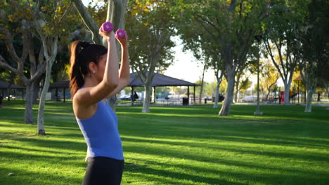 una hermosa y en forma joven hispana en el parque haciendo un ejercicio de prensa de hombro con mancuernas a cámara lenta