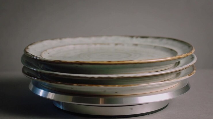 Rotating silver turntable causing three stacked ceramic plates rotating on tabletop, showing chips