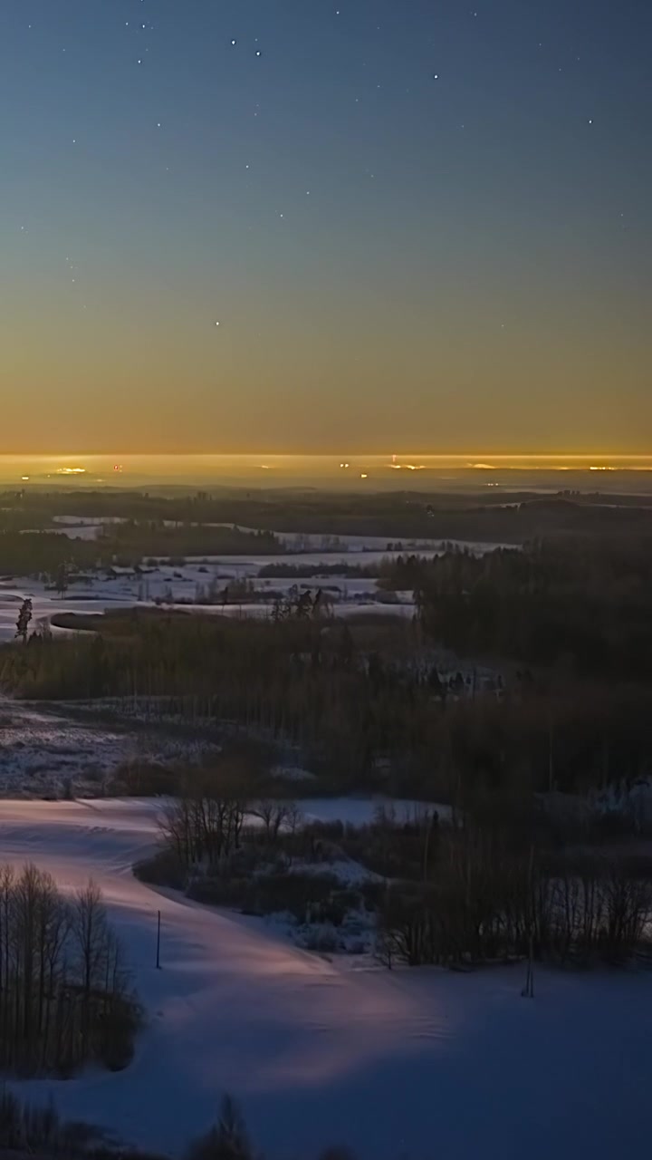 Cielo notturno su paesaggio innevato con luci della città che brillano all'orizzonte in timelapse invernale
