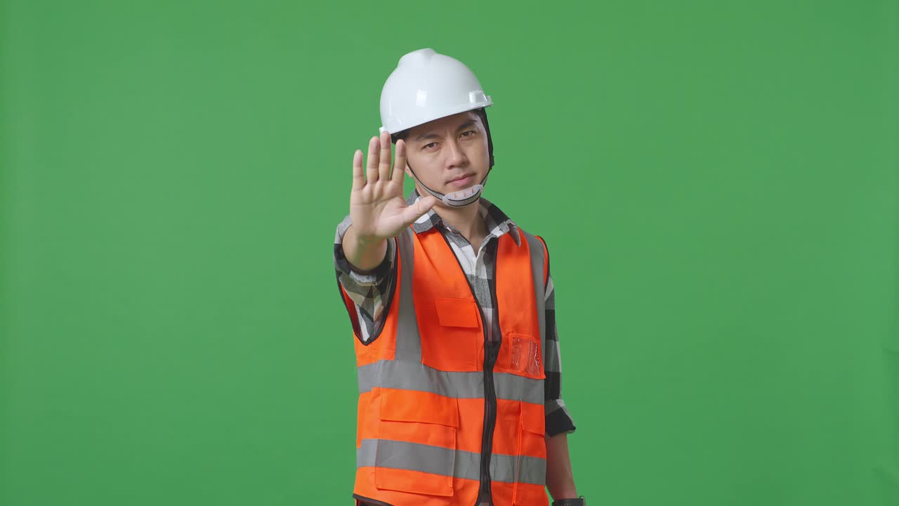 Asian Male Engineer With Safety Helmet Disapproving With No Hand Sign While Standing In The Green Screen Background Studio