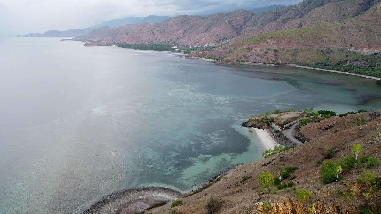 elevándose sobre un escarpado paisaje costero de montañas y colinas durante la estación seca con aguas cristalinas del océano en la isla tropical de timor leste, sudeste de asia