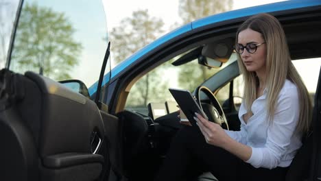 attractive businesswoman sitting in electric car, drinking coffee and looking at tablet. modern businesswoman having coffee break in car
