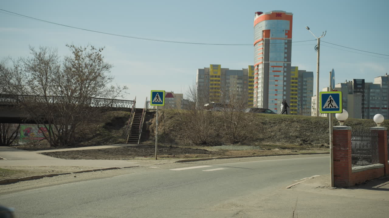 близкий вид городского пейзажа с знаком пешеходного перехода, машиной, поворачивающейся на дороге, и многоэтажными зданиями на заднем плане, с двумя людьми, идущими вместе