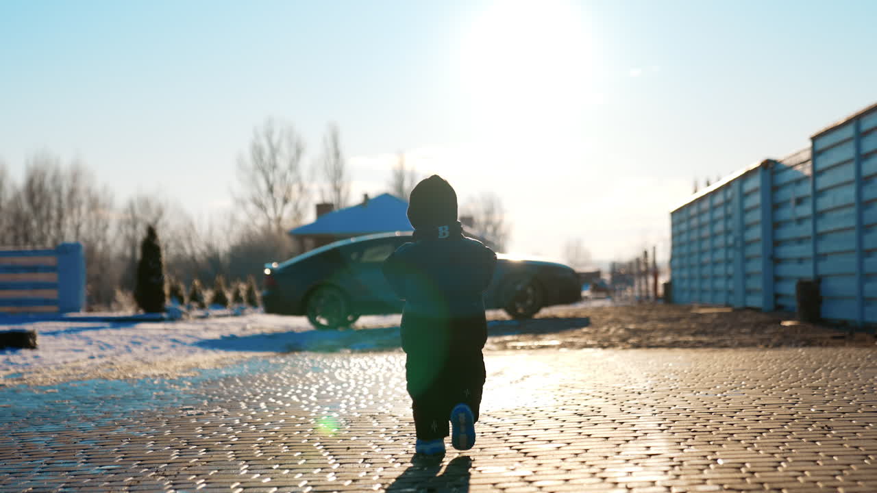 Small baby boy wearing black blazer, cap, sunglasses and pants outdoors. Lovely kid walks to the car standing at backdrop.