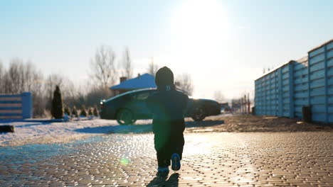 small baby boy wearing black blazer, cap, sunglasses and pants outdoors. lovely kid walks to the car standing at backdrop.