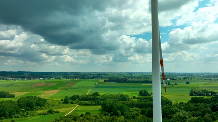 Luftoptagelse med en vindmølle mod en baggrund af frodige grønne marker og en landsby i det fjerne