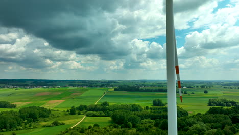 Aerial-footage-featuring-a-wind-turbine-against-a-backdrop-of-lush-green-fields-and-a-village-in-the-distance