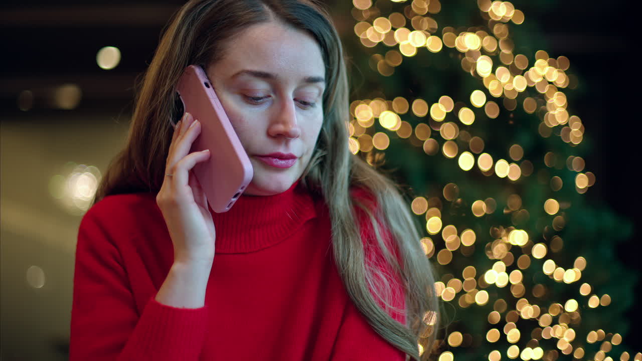 Woman in red sweater talking on the smartphone with christmas tree on background