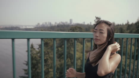 Medium-Closeup-shot-of-attractive-asian-girl-running-on-Lions-Gate-bridge-with-Vancouver-downtown-in-background,-Slowmo