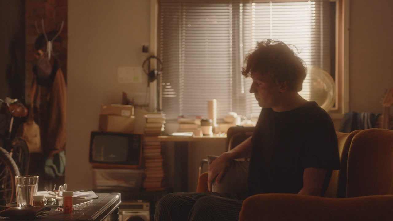 지친 젊은이가 아래층으로 내려가, 망진창한 거실에서 소파에 앉아