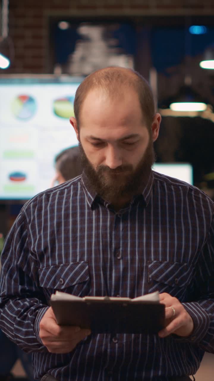 Vertical video: Employee reading report, holding clipboard, looking at camera, smiling