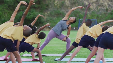 maestra de raza mixta que muestra a un grupo diverso de escolares ejercicios de estiramiento de yoga al aire libre