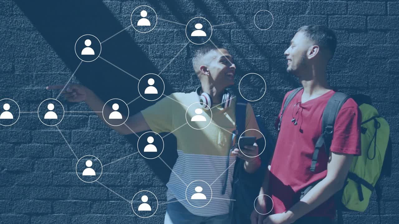 Two men leaning on brick wall, left man pointing and tapping phone, creating social network overlay