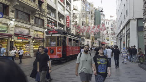 a bustling street scene on istiklal avenue in istanbul, featuring a historic red tram and numerous pedestrians.