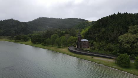 Aerial-view-of-the-Chapel-of-Nossa-Senhora-das-VitÃ³rias,-a-small-funerary-chapel-on-the-southwestern-corner-of-Lagoa-das-Furnas-in-the-civil-parish-of-Furnas-on-the-Azorean-island-of-SÃ£o-Miguel-2