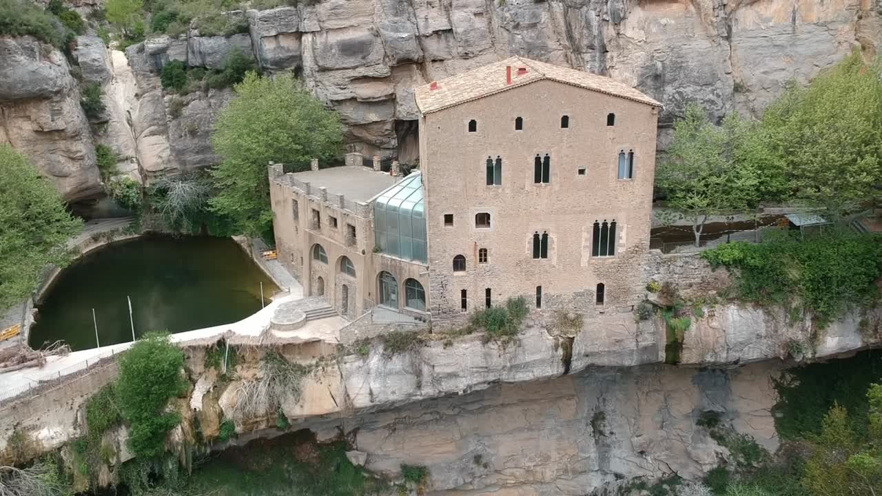 vistas aéreas de una cascada con una cueva y un edificio antiguo en cataluña, españa