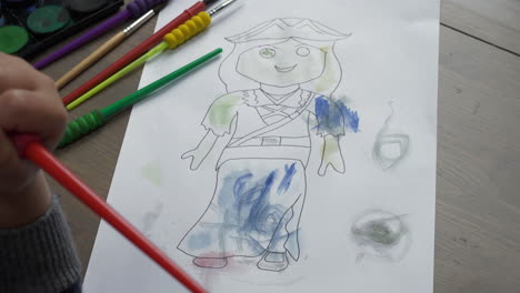 a mid shot of a young child colouring in a female figure with watercolours, sat at a desk