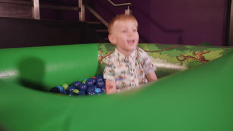 a young boy plays in ball pit and throws balls around whilst smiling