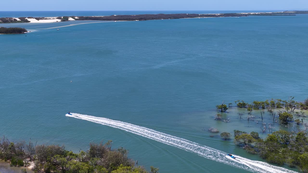 Bidikan drone sudut tinggi dari speedboat putih yang melaju melalui perairan muara pantai biru yang tenang