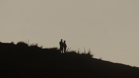 two unrecognizable people in silhouette standing on hill slope, sunset