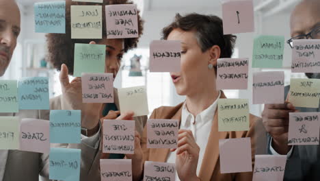 corporate business team using sticky notes brainstorming problem solving strategy on glass whiteboard working on deadline in office meeting