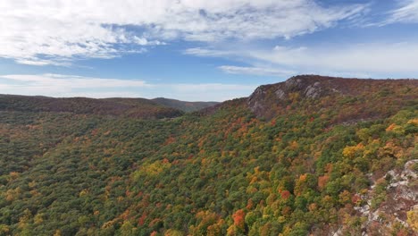 An-aerial-view-high-over-the-mountains-in-upstate-NY-during-the-fall-foliage-change,-on-a-beautiful-day-with-white-clouds