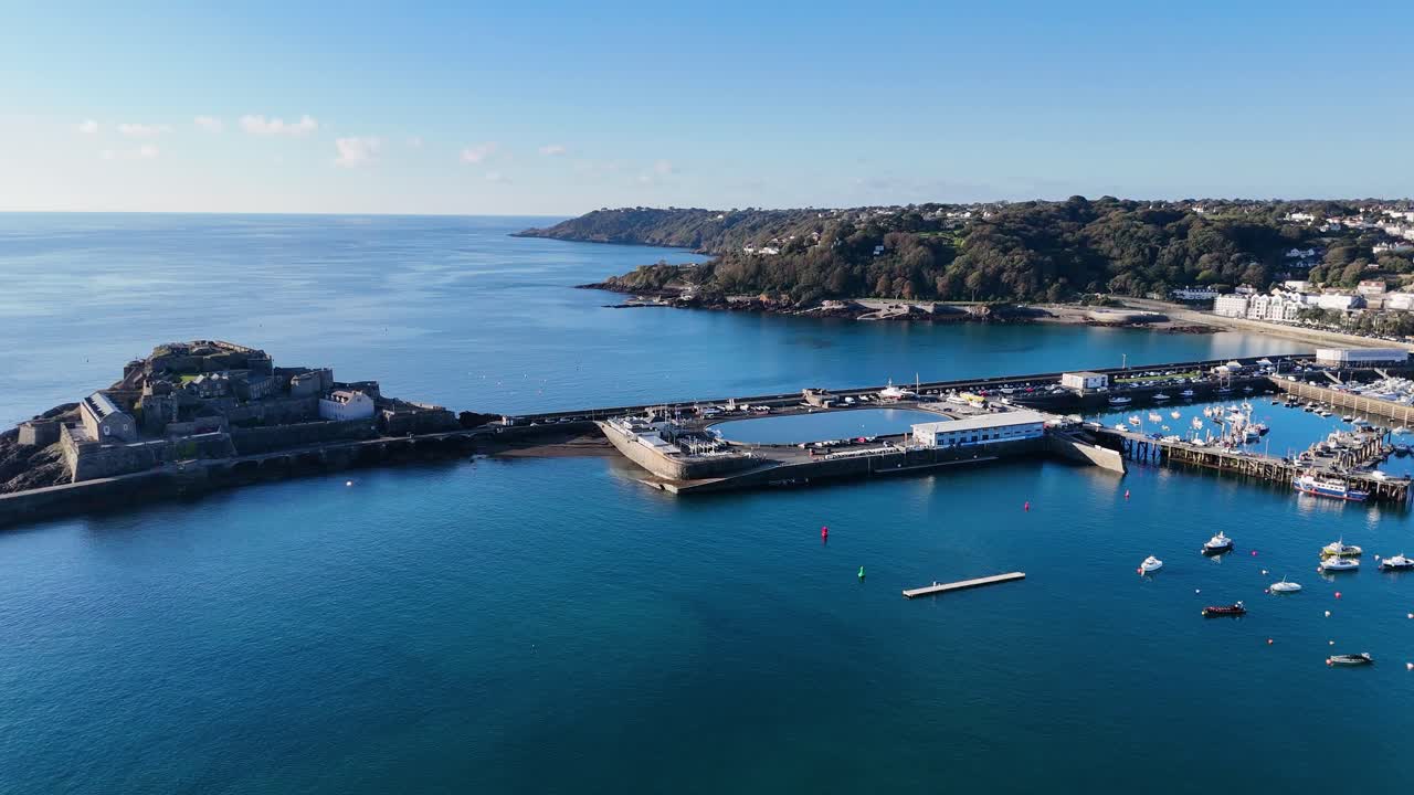 St Peter Port, Guernsey, revela filmagem de drone do Castelo Cornet e do porto com vistas para St Martin, com um mar calmo azul profundo deslumbrante sob o sol do final da tarde.