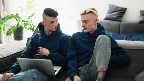 una pareja gay amorosa pasa tiempo en casa, usando una computadora portátil en el sofá de la sala de estar